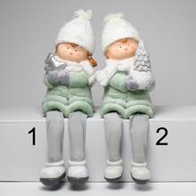 Dve deti s visiaci nohami v tyrkysovej farbe, oblečené v zimných bundách a čiapkach.