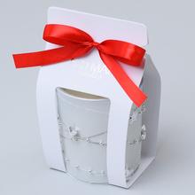 Bílá vonná svíčka ve skleněném obalu s červenou stuhou.