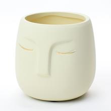 Bílý květináč s otvorem ve tvaru obličeje.