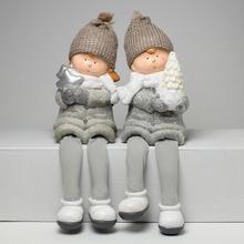 Dvě děti se šedýma nohama, oblečené v zimních čepicích a šálách, drží v rukou vánoční dekorace.