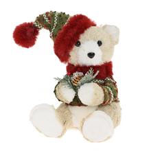 Sedící medvěd v krémové barvě, s čepicí a svetrem, držící šišku.